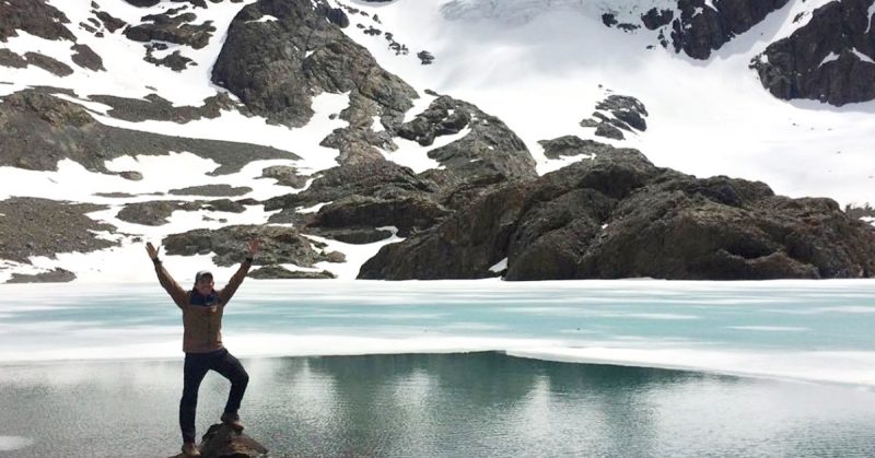 Turista sozinho com um pé em cima da pedra e ao fundo a laguna e montanhas cobertas com o pico de neve | Brasileiros em Ushuaia
